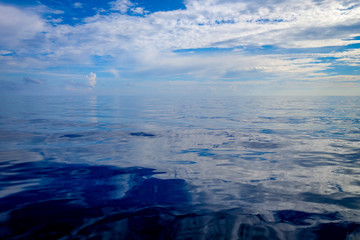 View of a calm ocean with an endless, undefined horizon, merging into the blue sky and white...