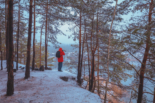 A man standing on the covered with snow rocky lakeshore in winter and looking at the beautiful lake