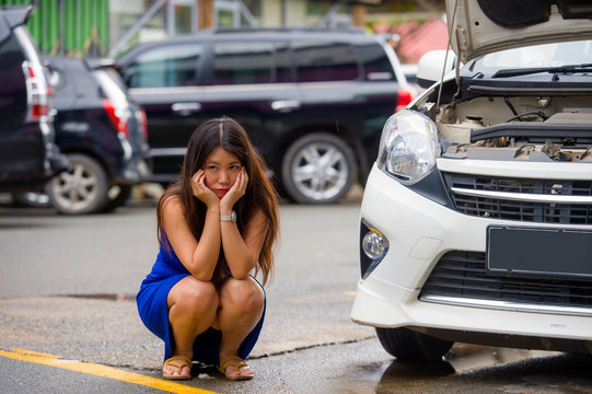 Worried Asian Japanese Woman In Stress Stranded On Roadside With Car Engine Failure Having Mechanic Problem Needing Repair Service Squating On Street Feeling Upset