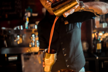 Expert barman making cocktail at nightclub.  Bartender preparing red cocktail at cocktail glass at the bar. Preparing of cosmopolitan cocktail. Red alcoholic drink in glasses on bar.