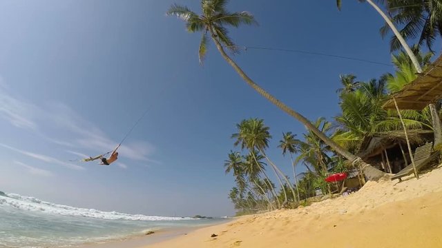 A man swinging on the palm tree on the white beach. Exotic vacation holidays spending concept.