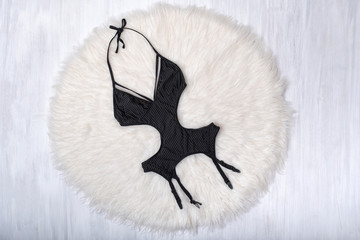 Black bodysuit with suspenders for stockings on white fur. Fashionable concept