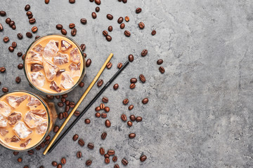 Cold brewed iced coffee in tall glass with coffee beans and straws on grey concrete background. Chocolate, vanilla, caramel or cinnamon iced coffee in tall glass. Top view with copy space for text.