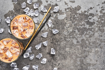 Cold brewed iced coffee in tall glass with ice and straws on wet grey concrete background. Chocolate, vanilla, caramel or cinnamon iced coffee in tall glass. Top view with copy space for text.