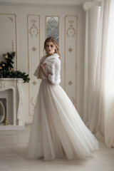 Beautiful bride in a wedding dress and white fur cape. Spinning in a dress. Fluffy dress. Interior Studio.