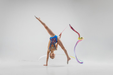 The portrait of beautiful young brunette woman gymnast training calilisthenics exercise with blue ribbon on white studio background. Art gymnastics concept. Caucasian model in full height