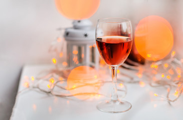 A glass of red wine on the white table with warm bokeh lights big and small. Blurred decorations. Home ambience