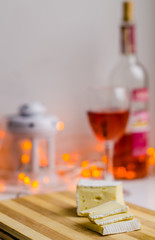 Naklejka na ściany i meble Slices of camembert or brie cheese on the white table with a bottle and a glass of red wine on the blurred background with bokeh. Concept of celebration. Delicatessen 