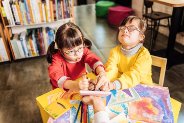 Dark-haired sunny children wearing glasses playing tricks while drawing