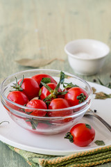 Red salted cherry tomatoes in a round glass bowl on an old wooden table. 