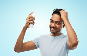 grooming, hairstyling and people concept - happy smiling indian man applying hair spray over blue background