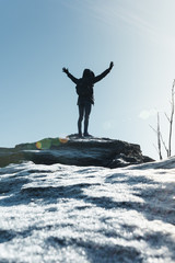 Cheering woman hiker open arms at mountain peak backlit with heavy lensflare and ice crystalls in the foreground.