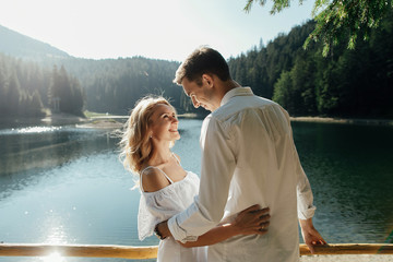 Young pretty couple hugging and smiling at the lake at sunset