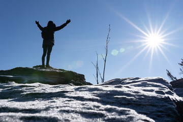 Cheering woman hiker open arms at mountain peak backlit with heavy lensflare and ice crystalls in the foreground.