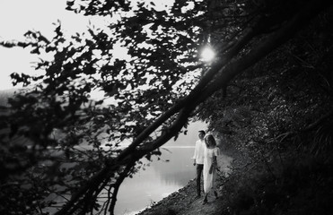Fototapeta premium Young pretty couple hugging and smiling at the lake at sunset