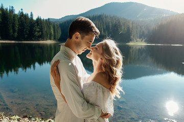Young pretty couple hugging and smiling at the lake at sunset
