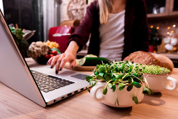 women in the kitchen searching for recipes on his laptop with food ingredients and fresh...