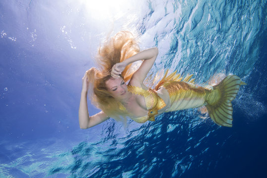 Golden-haired mermaid swims underwater surface in blue water, Indian Ocean, Maldives