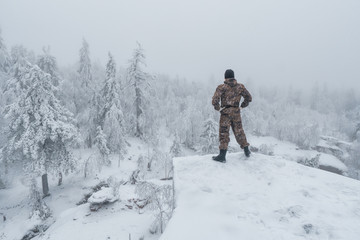 Man hiker standing back on rock in winter mountain landscape, success