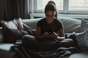 Obraz premium Smiling girl sitting on the couch looking at mobile phone