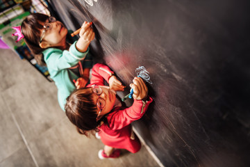 Obraz premium Top view of two sunny children wearing glasses drawing on blackboard