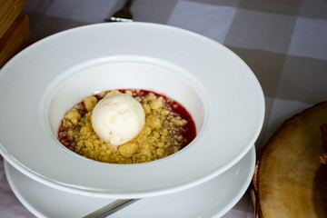 strawberry crumble with vanilla ice cream on a white plate.