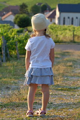 Little girl in a hat stands against a background of vineyards