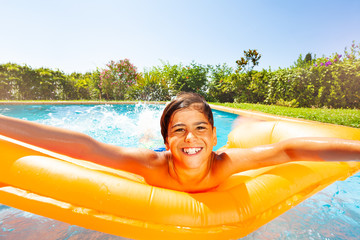 Funny boy swimming on air mattress in outdoor pool