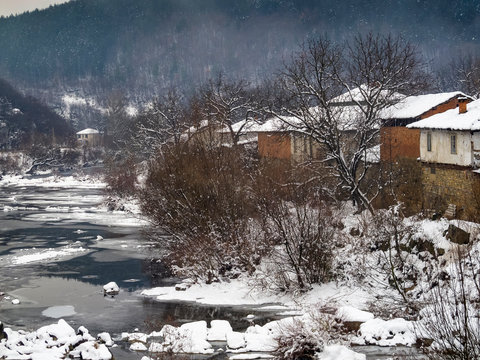 Picturesque elevated snowy rural view from a bridge to the winter Vidima River and old riverbank houses at the Bulgarian village of Debnevo, Central-North Bulgaria