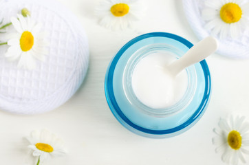 Ligh blue glass jar with white facial cream/mask. Yogurt beauty treatment. hamomile flowers on the white background. Top view, copy space.  