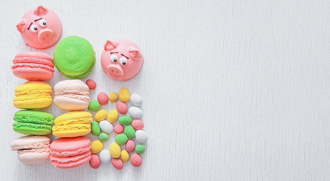 Marzipan in the shape of the symbol of the new year - pink pig, sweet delicate macaroons, marshmallows, peanuts in sugar pastel colors on a light background with space for text
