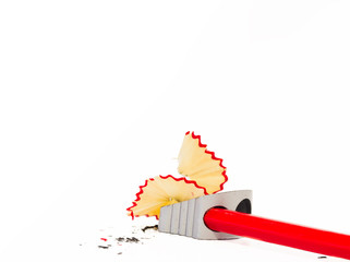 Close up view of a red pencil being sharpened in a metallic pencil sharpener with wood shavings...