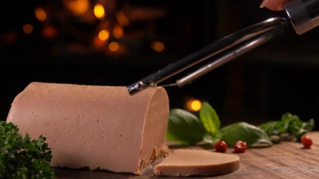 Special knife cuts a slice of foie gras in the background of a burning fireplace