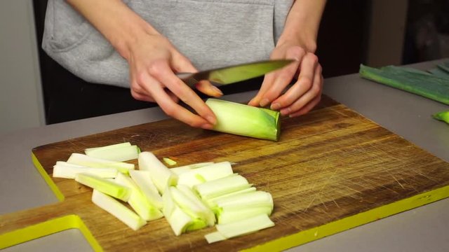 Closeup of a woman peeling and cutting leeks over a wooden table