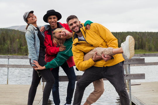 Finland, Lapland, Portrait Of Happy Playful Friends On Jetty At A Lake