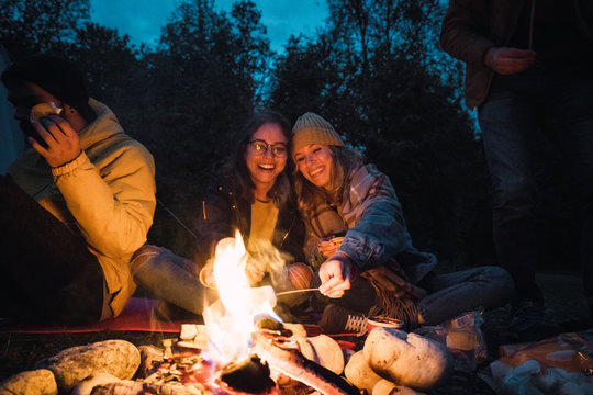 Group of friends sitting at a campfire, roasting marshmallows - Powered by Adobe