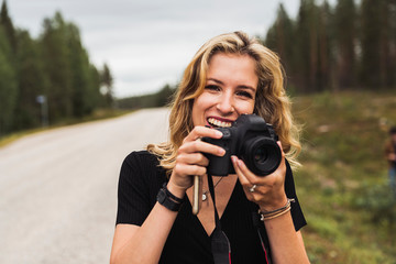 Finland, Lapland, portrait of happy young woman holding camera at country road