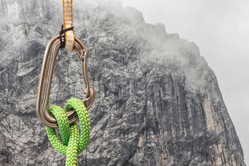 A carabiner with a climbing rope and sling on rock wall background. Mountaineering and climber...
