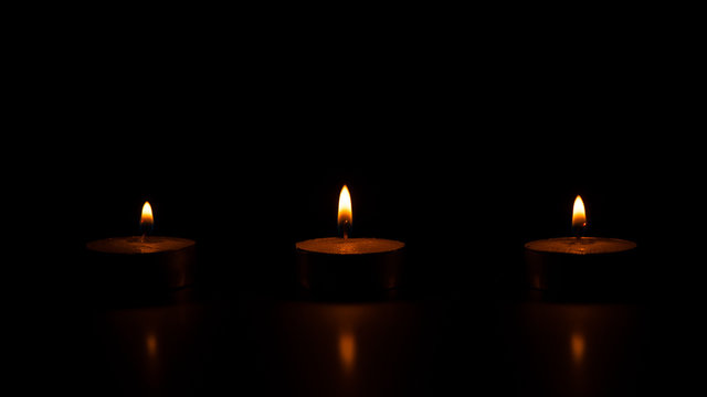 Three lighted wax candles on a black background