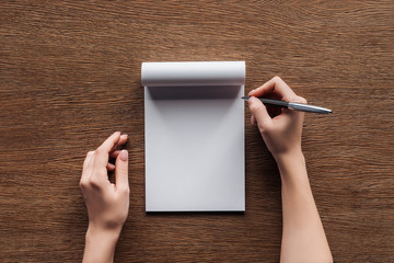 cropped view of person holding pen over blank notebook on wooden background