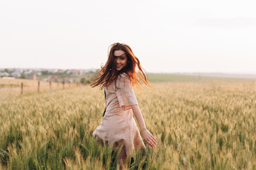 The beautiful girl in the dress is having fun on the field at sunset. Female psychology. The concept of freedom
