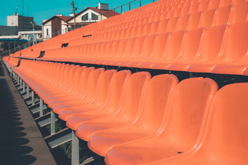 Naklejka premium the rows of chairs of orange color leaving in the distance, the tinted photo, plastic seats for the audience under