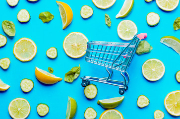 Above view at cutted lemons and limes and shopping cart on blue background