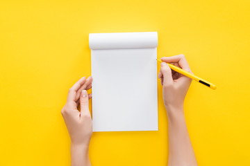  partial view person holding pen over blank notebook on yellow background - obrazy, fototapety, plakaty