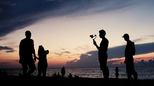 Silhouettes of tourists with technology on the background of a sunset on the sea