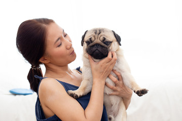 Beautiful Asian young woman playing with her dog and smile with dog pug breed looking in funny and serious face in bedroom,Friendship Concept