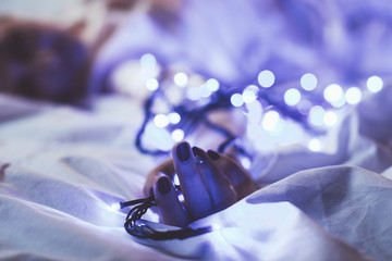 cropped shot of woman resting on bed with christmas festive lights around