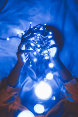 obscured view of woman holding blue lights in hands while lying on bed