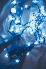 cropped shot of woman with bottle of champagne and glasses on bed with festive blue lights around