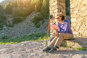 Woman hiker with book or map planning next trip, near the building of a hiking shelter in mountains